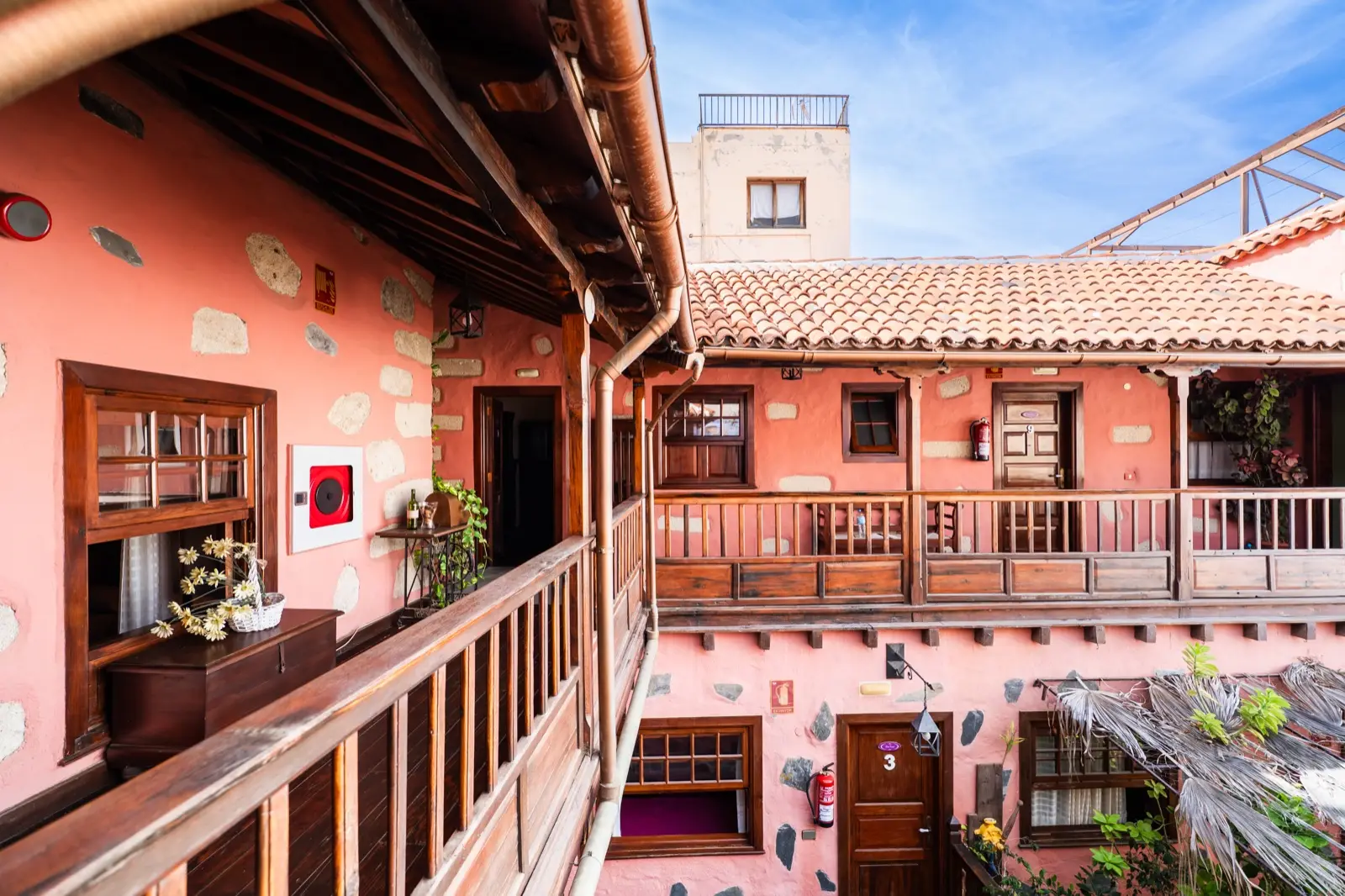 Galería de madera de la planta alta abierta al patio, con paredes rosadas, piedra vista y tejado de teja