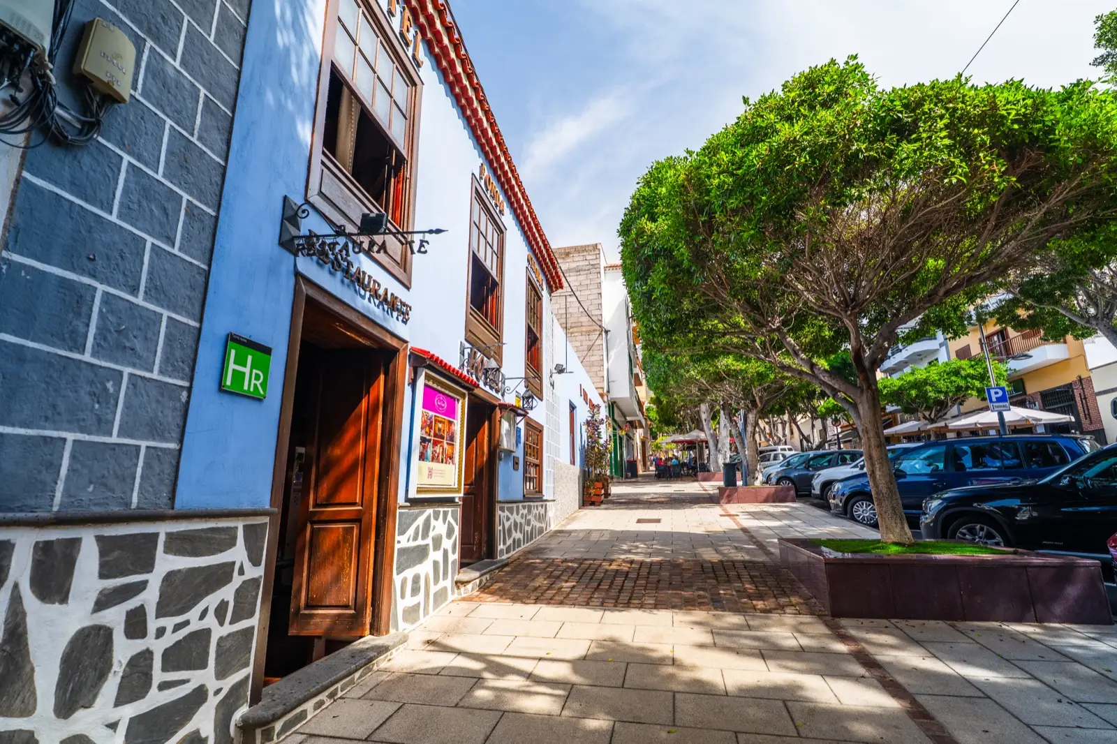 Fachada del hotel y la calle Grande de Adeje, con árboles y una acera amplia