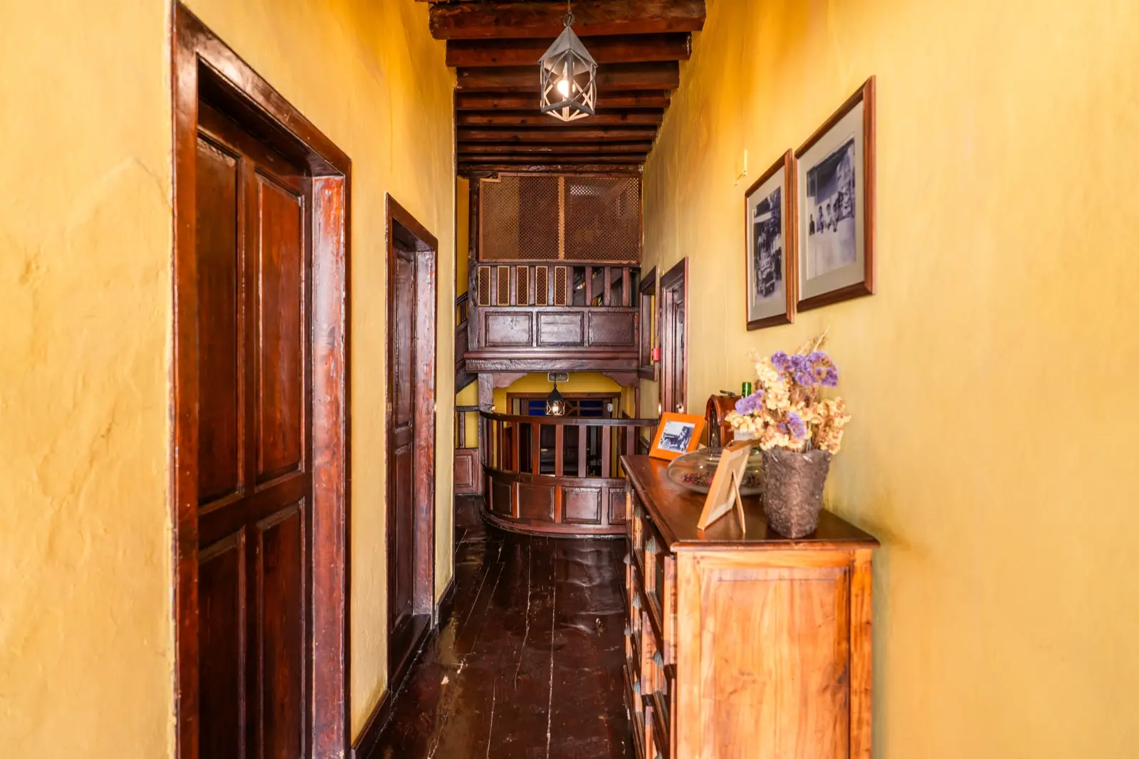 Pasillo con suelo de madera, puertas de madera, una cómoda y fotografías antiguas en las paredes amarillas