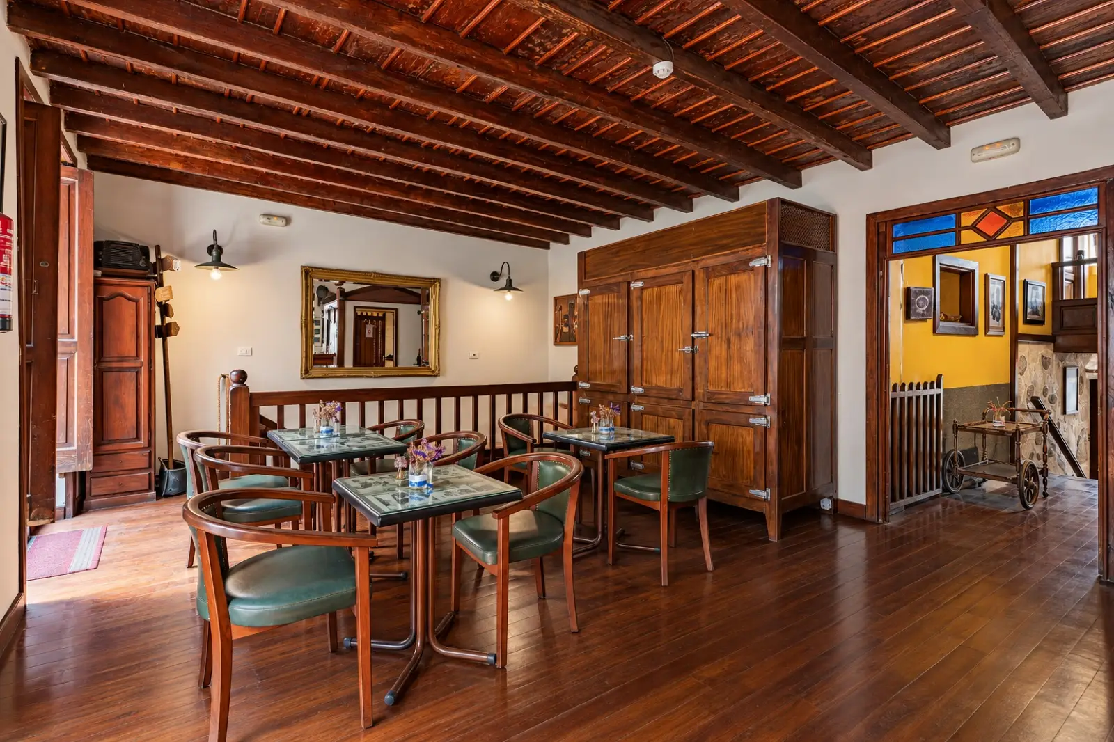 Sala con mesas y sillones de cuero verde, techo de vigas de madera, espejo dorado y una vidriera de colores sobre la puerta