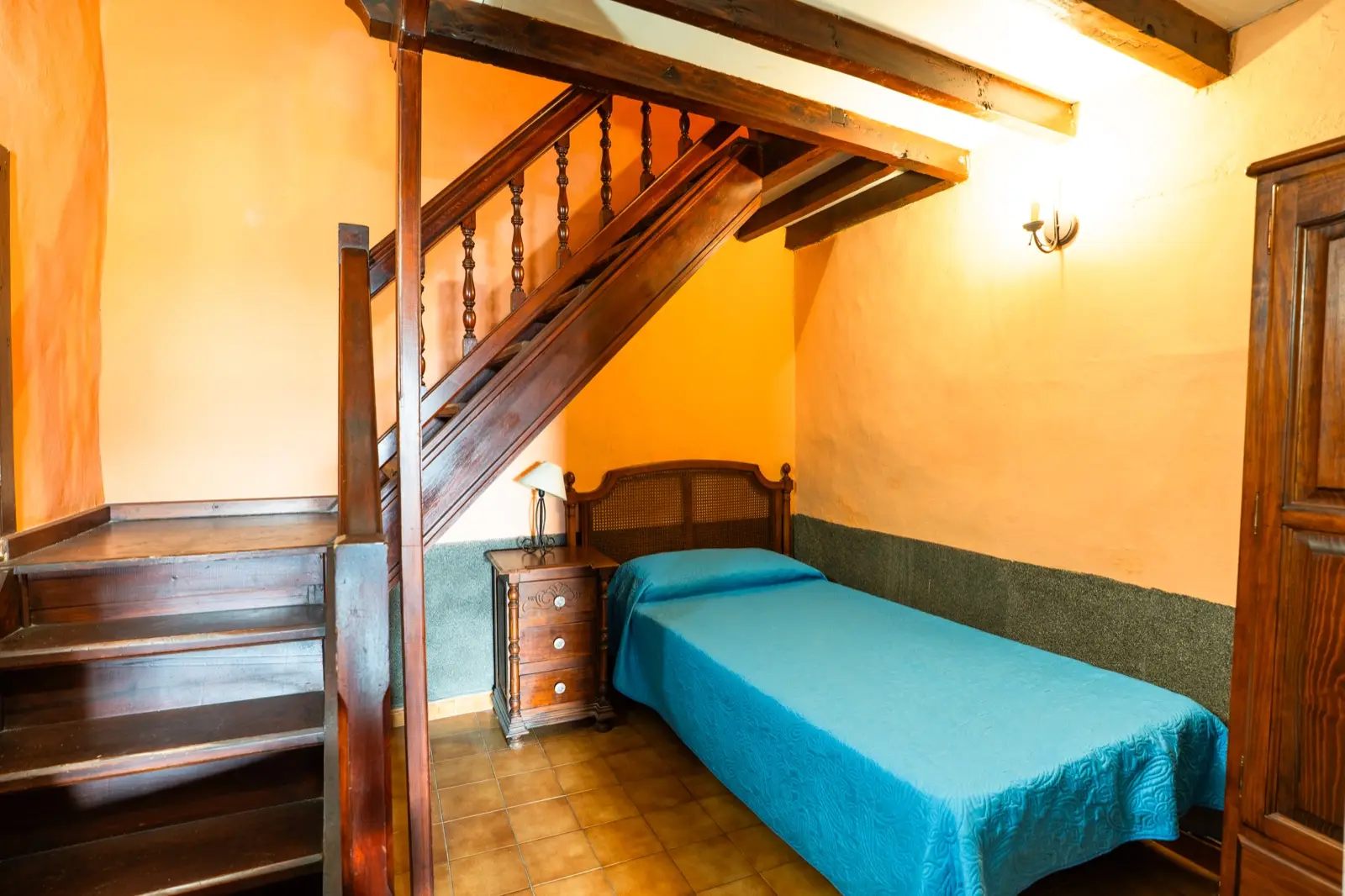 Habitación triple: cama individual con colcha azul junto a la escalera de madera interior de la habitación
