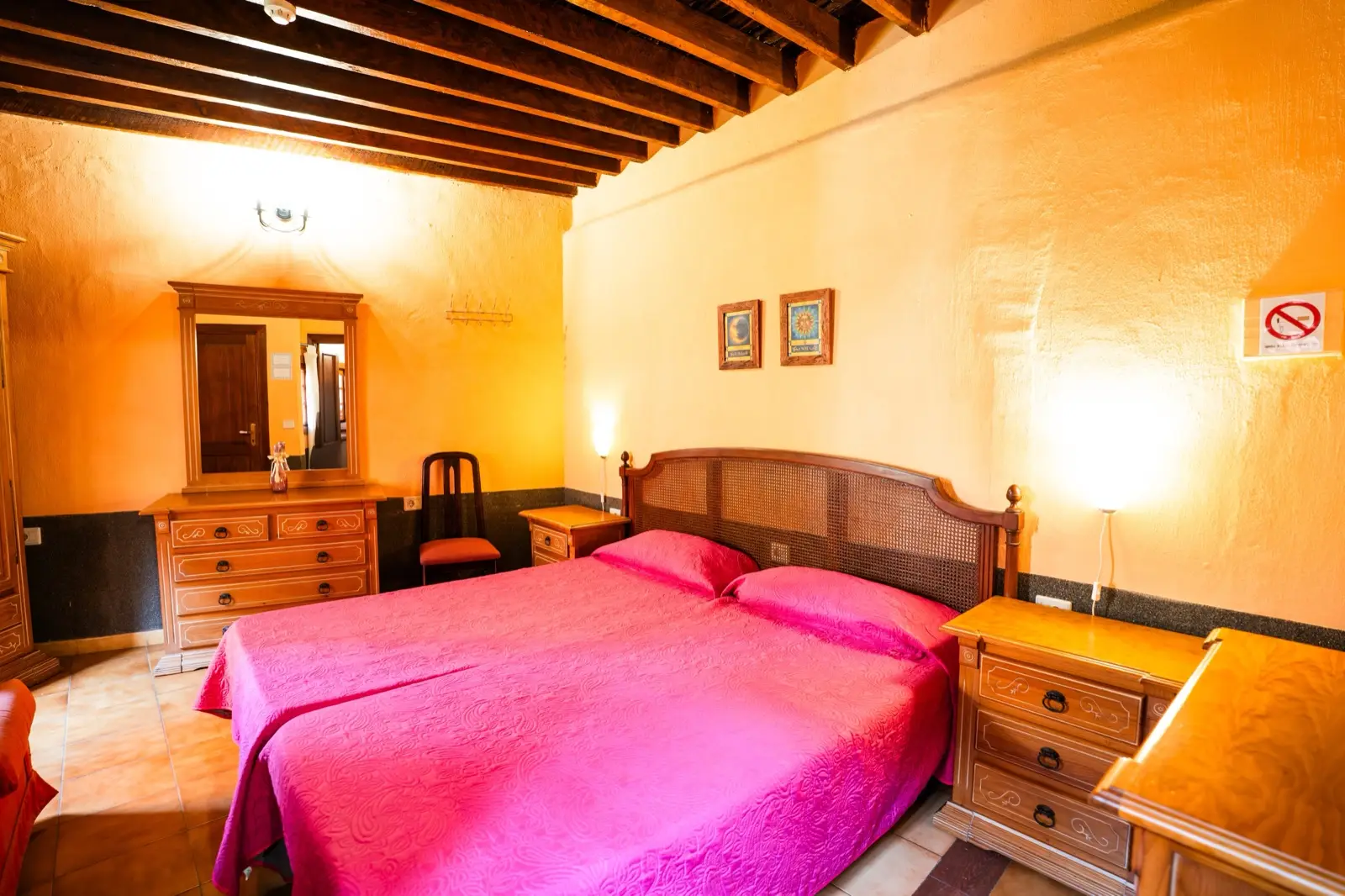 Habitación doble con dos camas individuales juntas, cabecero de rejilla, colchas fucsia, techo de vigas y paredes anaranjadas