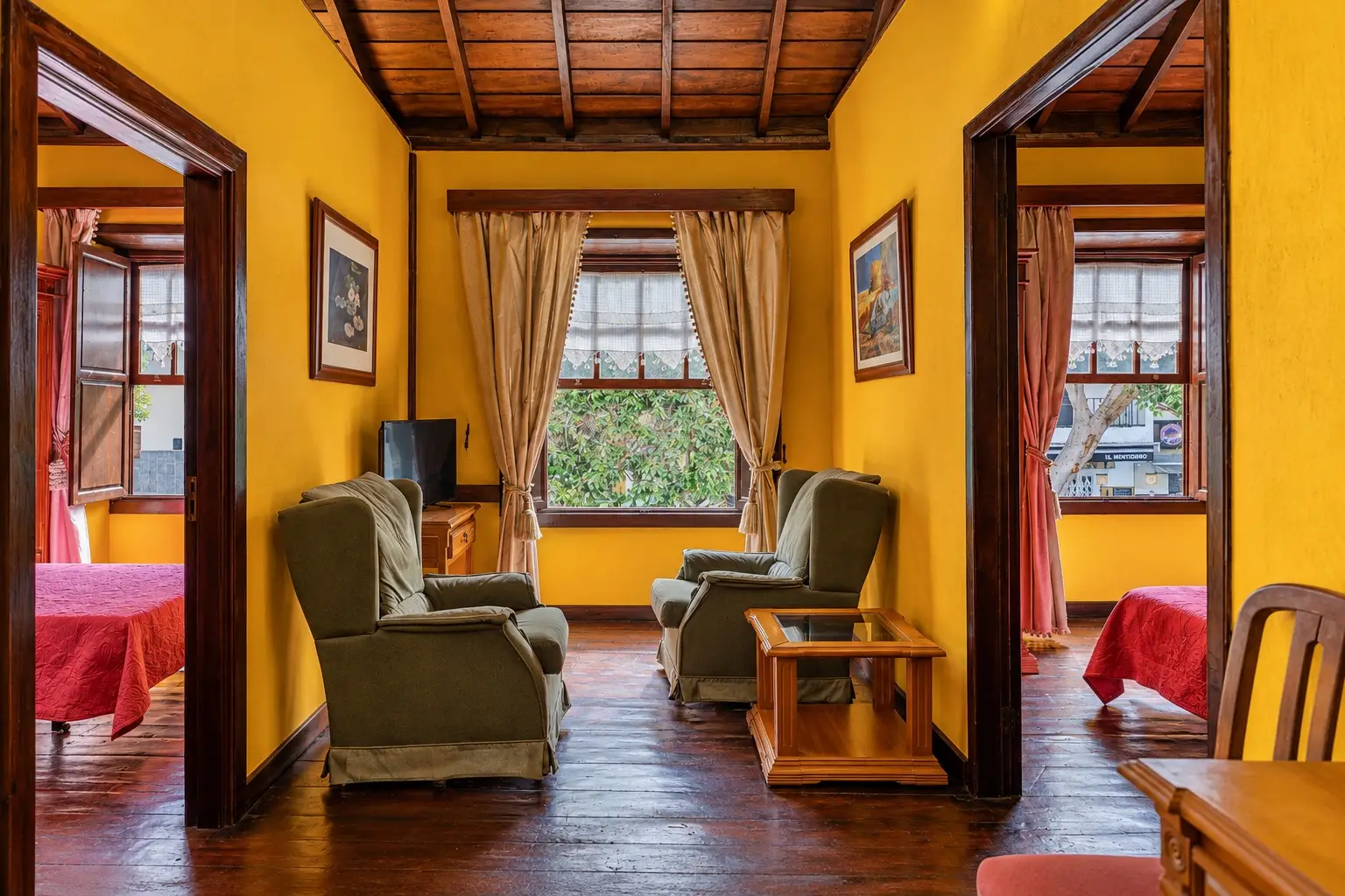 Habitación cuádruple: salita con dos sillones, mesa baja y ventana de madera, entre dos dormitorios