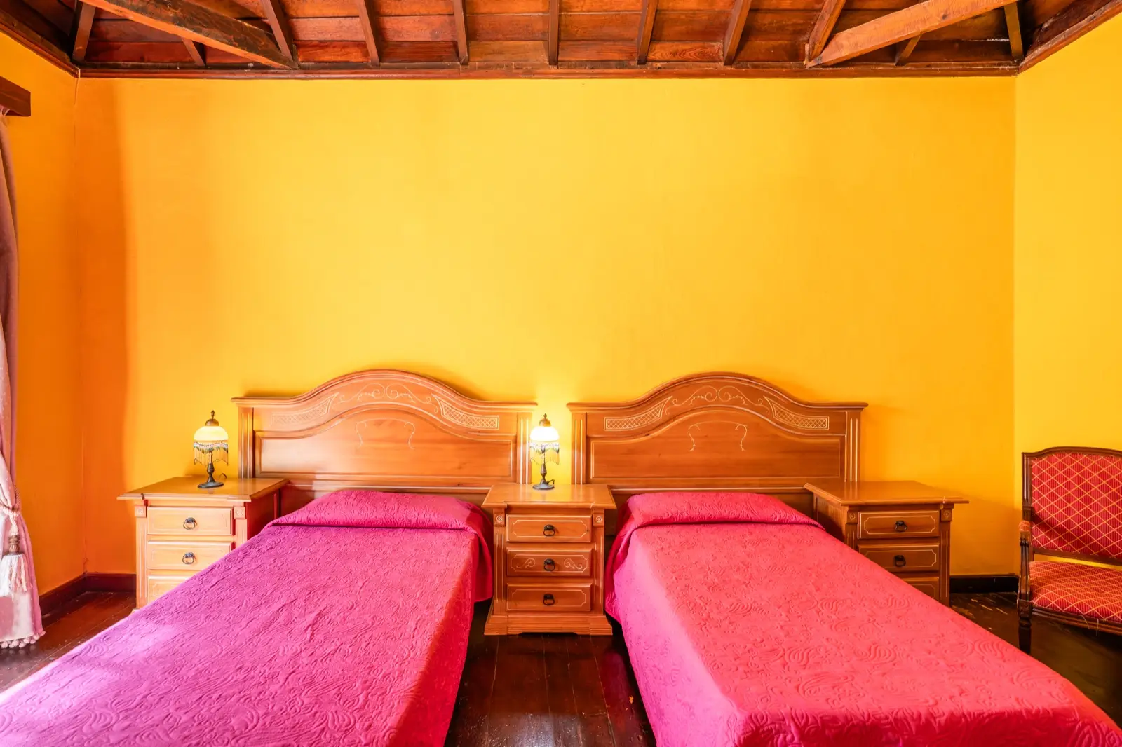 Habitación cuádruple: dormitorio con dos camas individuales de cabecero de madera, colchas fucsia, paredes amarillas y techo de madera