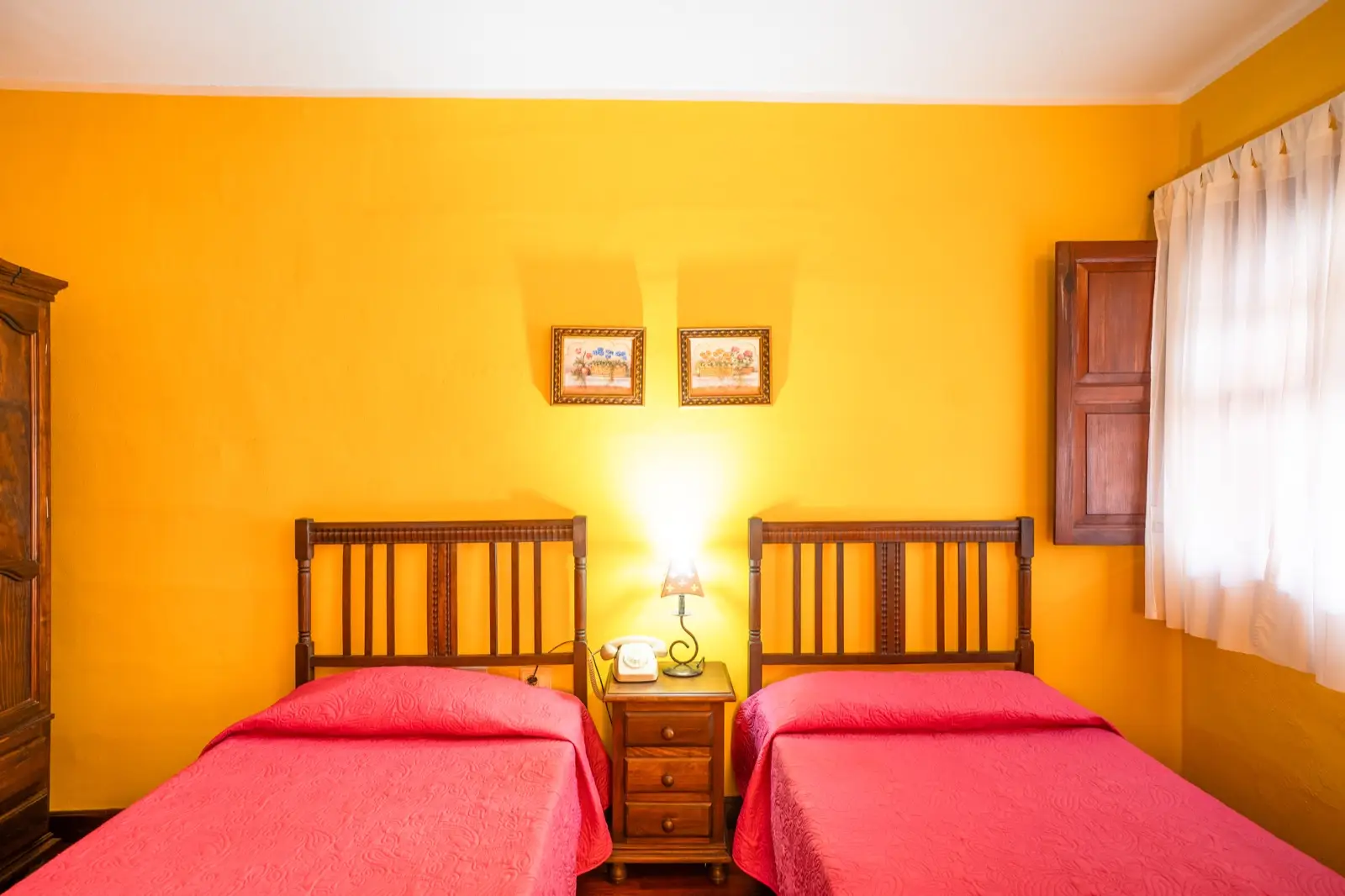 Habitación doble con dos camas individuales, cabeceros de madera torneada, colchas fucsia y paredes amarillas
