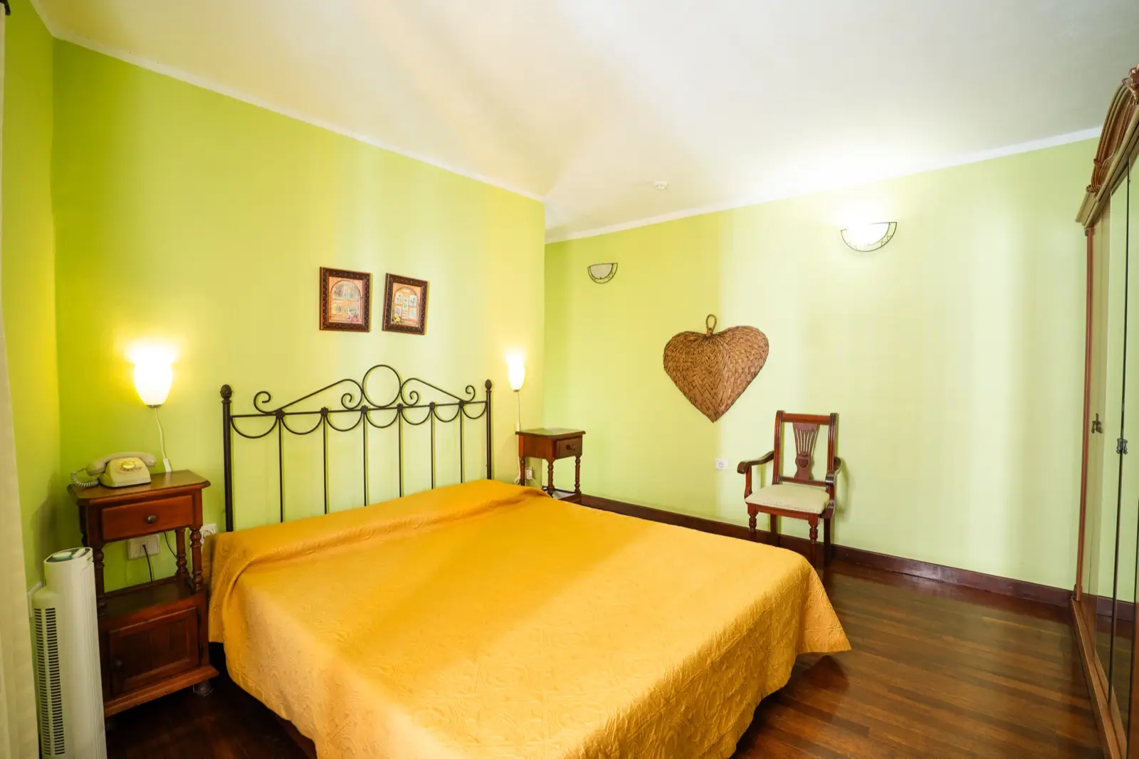 Habitación doble con cama de matrimonio, cabecero de forja, colcha dorada y paredes verde claro