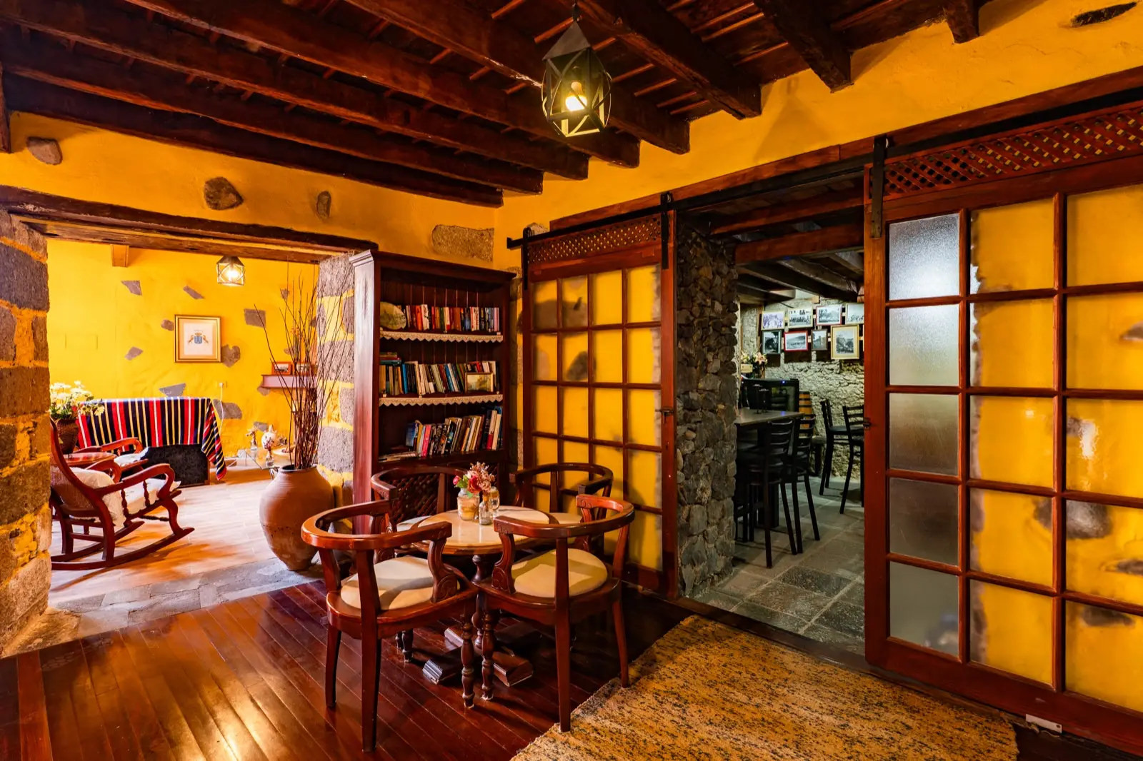 Rincón de lectura con estantería de libros y mesa con sillones de madera, junto a las puertas correderas que dan a la bodega