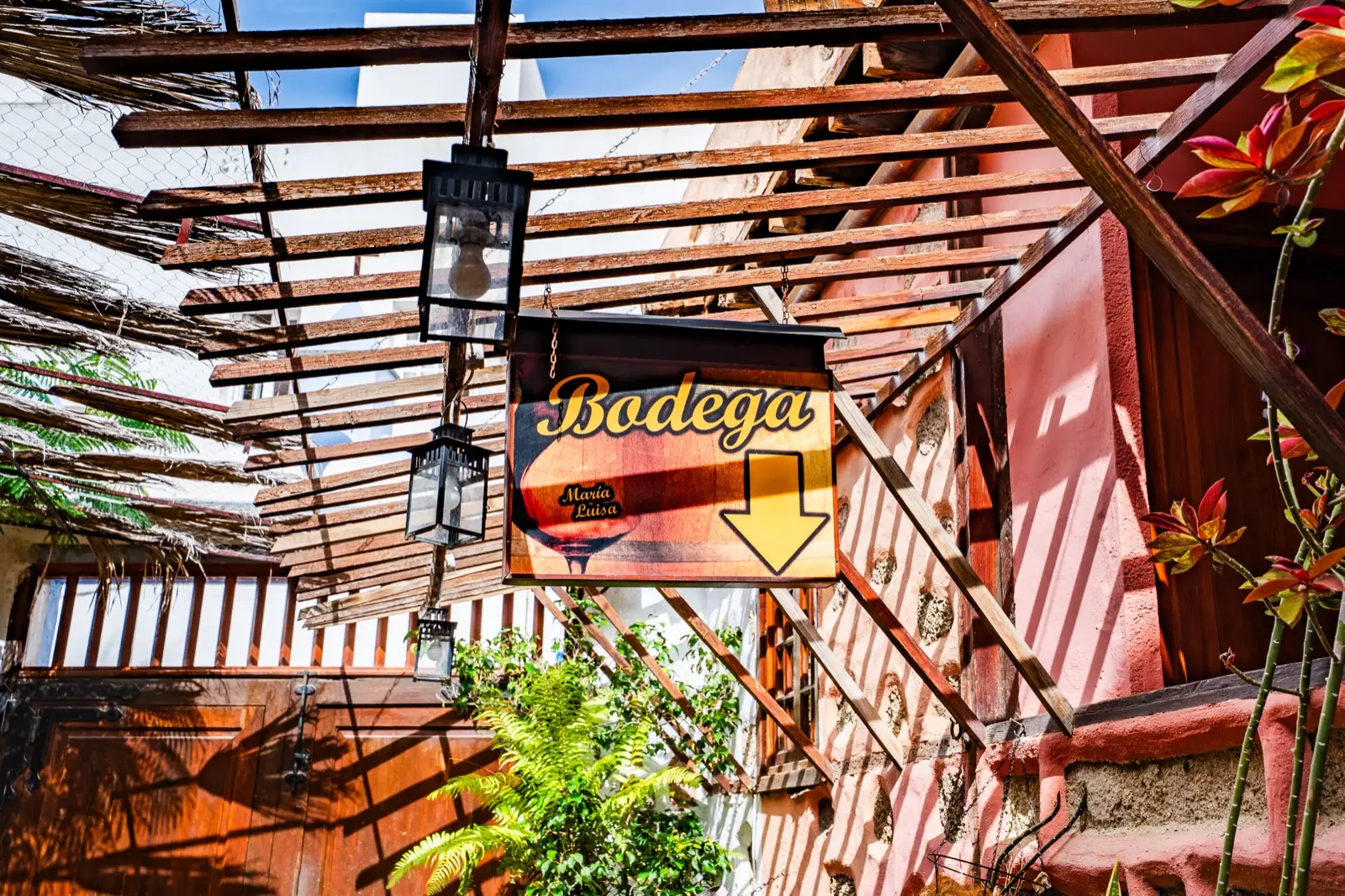 Pérgola de madera y cañizo con faroles y el cartel «Bodega» en el patio
