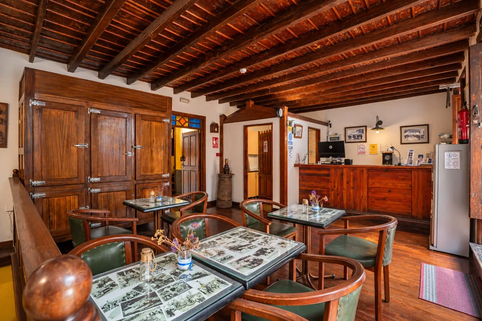 Recepción con mostrador de madera, mesas con sillones de cuero verde, un gran armario de madera y techo de vigas