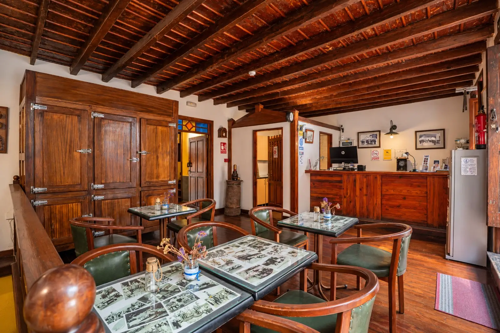 Recepción con mostrador de madera, mesas con sillones de cuero verde, un gran armario de madera y techo de vigas
