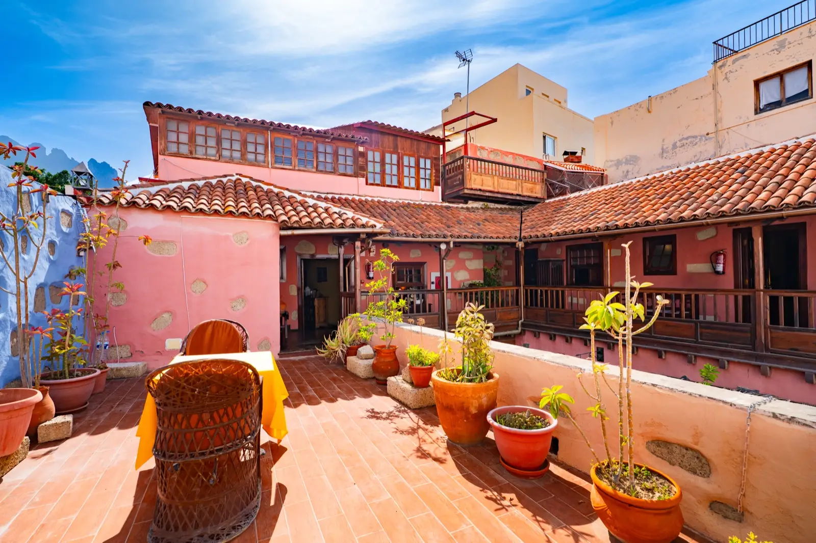 Solárium en la azotea con una mesa, sillones de mimbre y macetas, frente a los tejados de teja y las galerías de madera de la casona