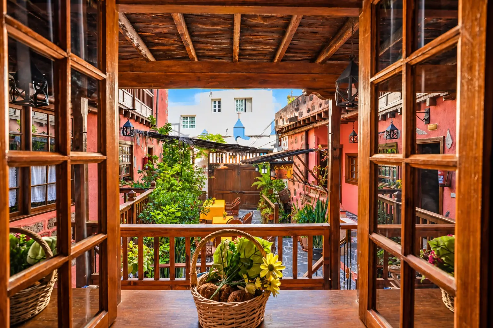 Ventana de madera abierta al patio, con galerías de madera y plantas, vista desde la habitación triple